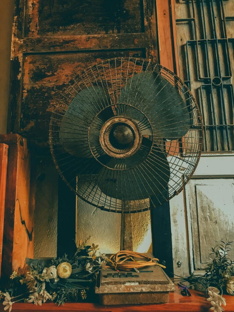 A rustic, vintage electric fan displayed indoors, showcasing its age and character with hints of rust and wear.